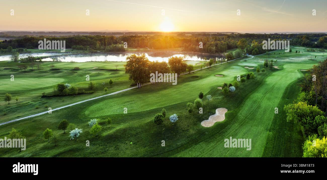 Golfplatz bei Sonnenuntergang mit wunderschönem Himmel und Sandfalle. Panoramablick auf das GolfFairway mit Bunker von der Drohne Stockfoto