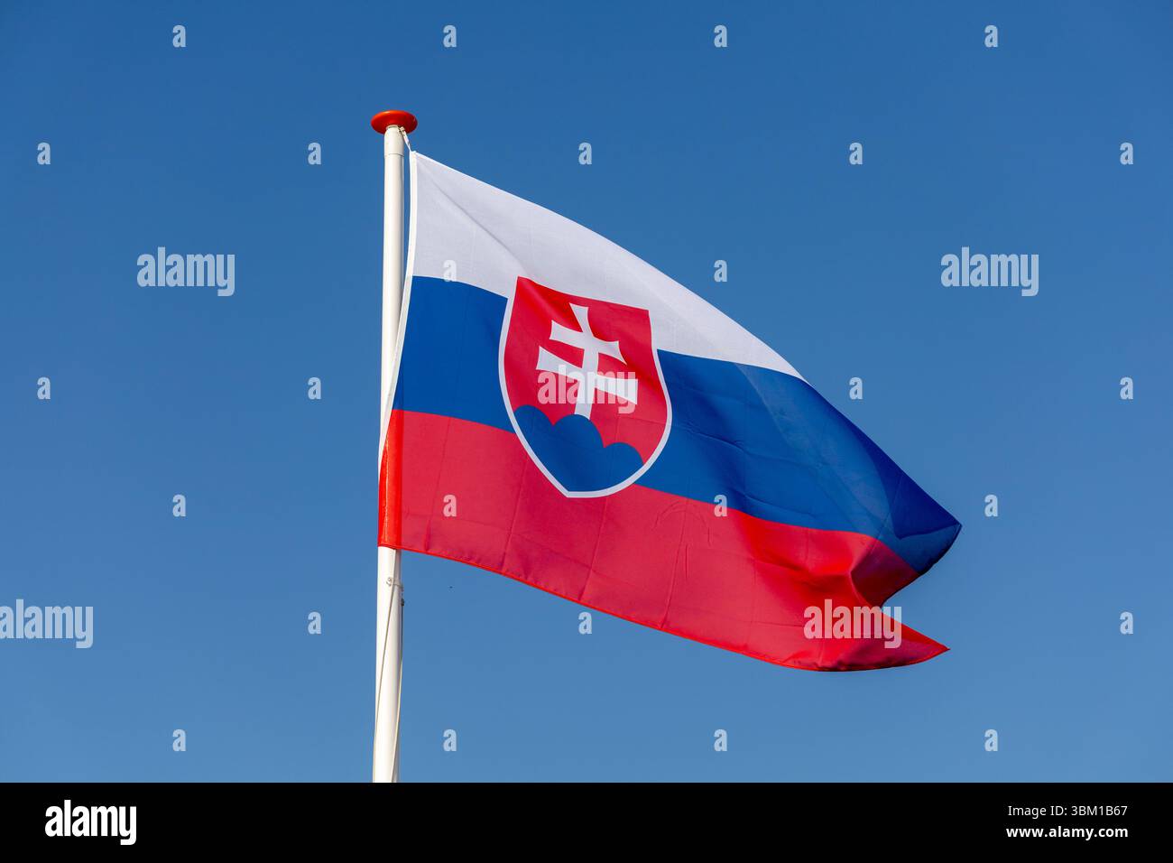 Die slowakische Flagge winkt im Wind gegen einen klaren blauen Himmel. Das Nationalwappen mit einem doppelten Kreuz auf drei Hügeln symbolisiert das ident der Slowakei Stockfoto