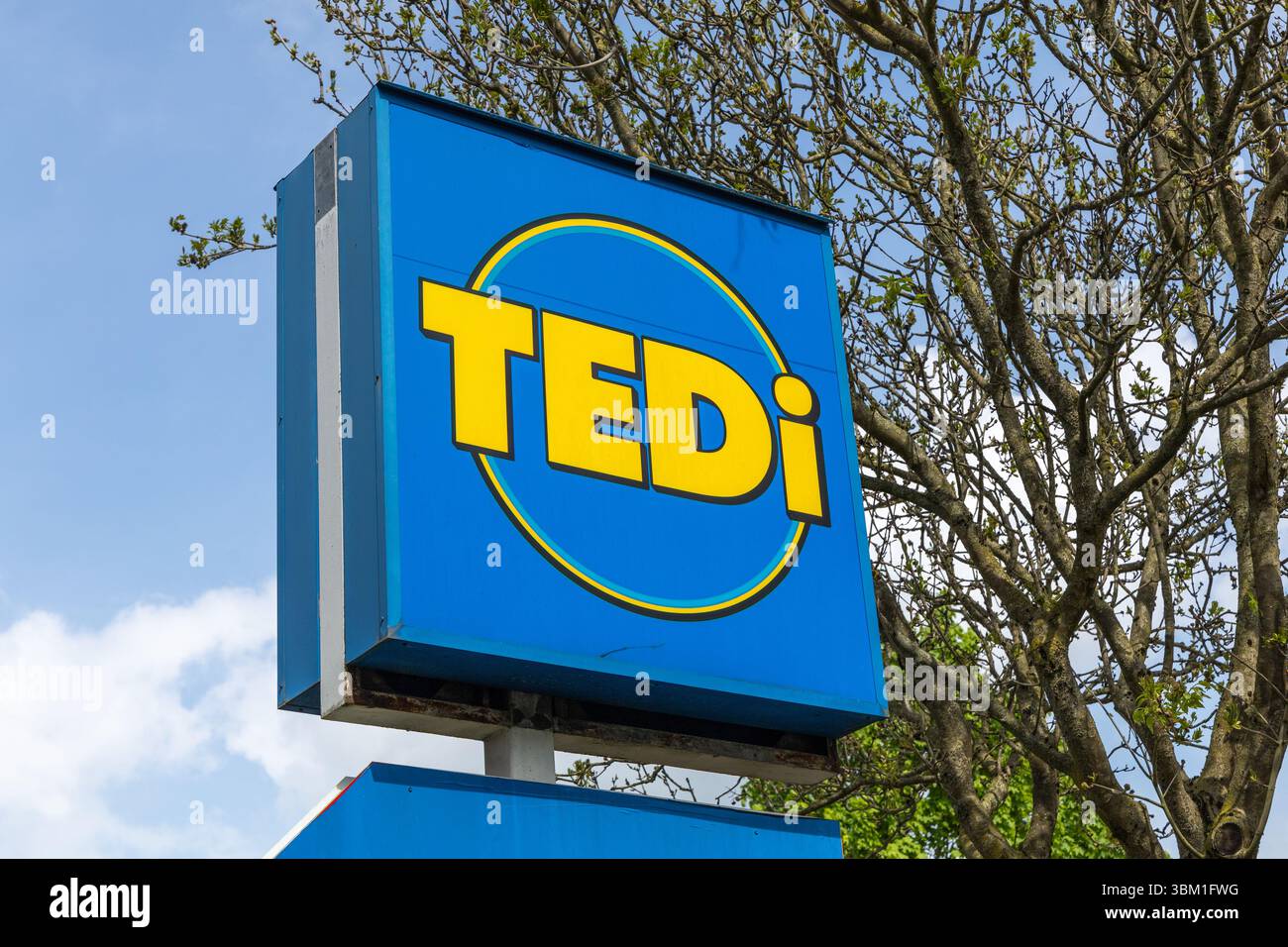 Ein hellblaues Tedi-Ladenschild mit gelber Schrift und kreisförmigem Design steht vor einem teilweise bewölkten Himmel. Kleve, Deutschland. 22. April 2025. Stockfoto