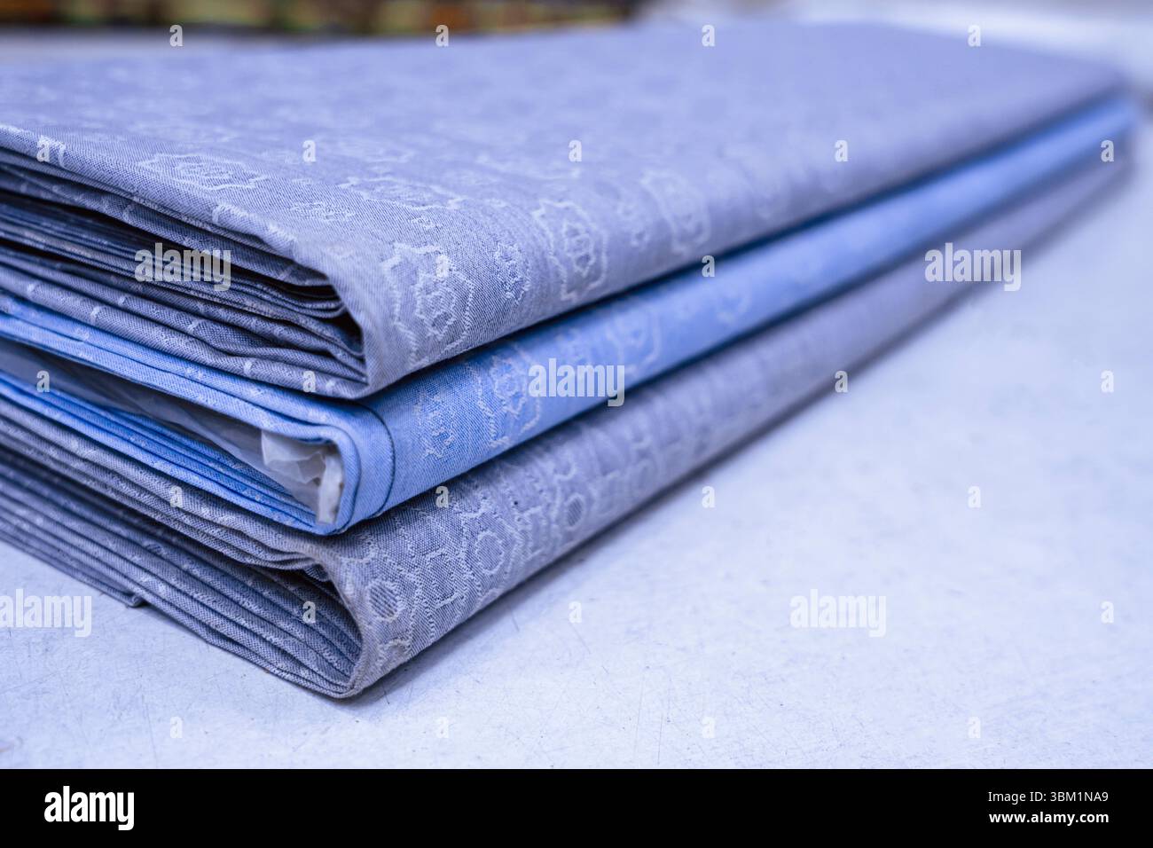 Ein Stapel von drei Schrauben aus luxuriösem blauem Baumwollgewebe mit dezentem geprägtem Muster liegt auf einer hellen Oberfläche auf. Die Stoffe sind mit verschiedenen SHA-Stoffen ausgestattet Stockfoto
