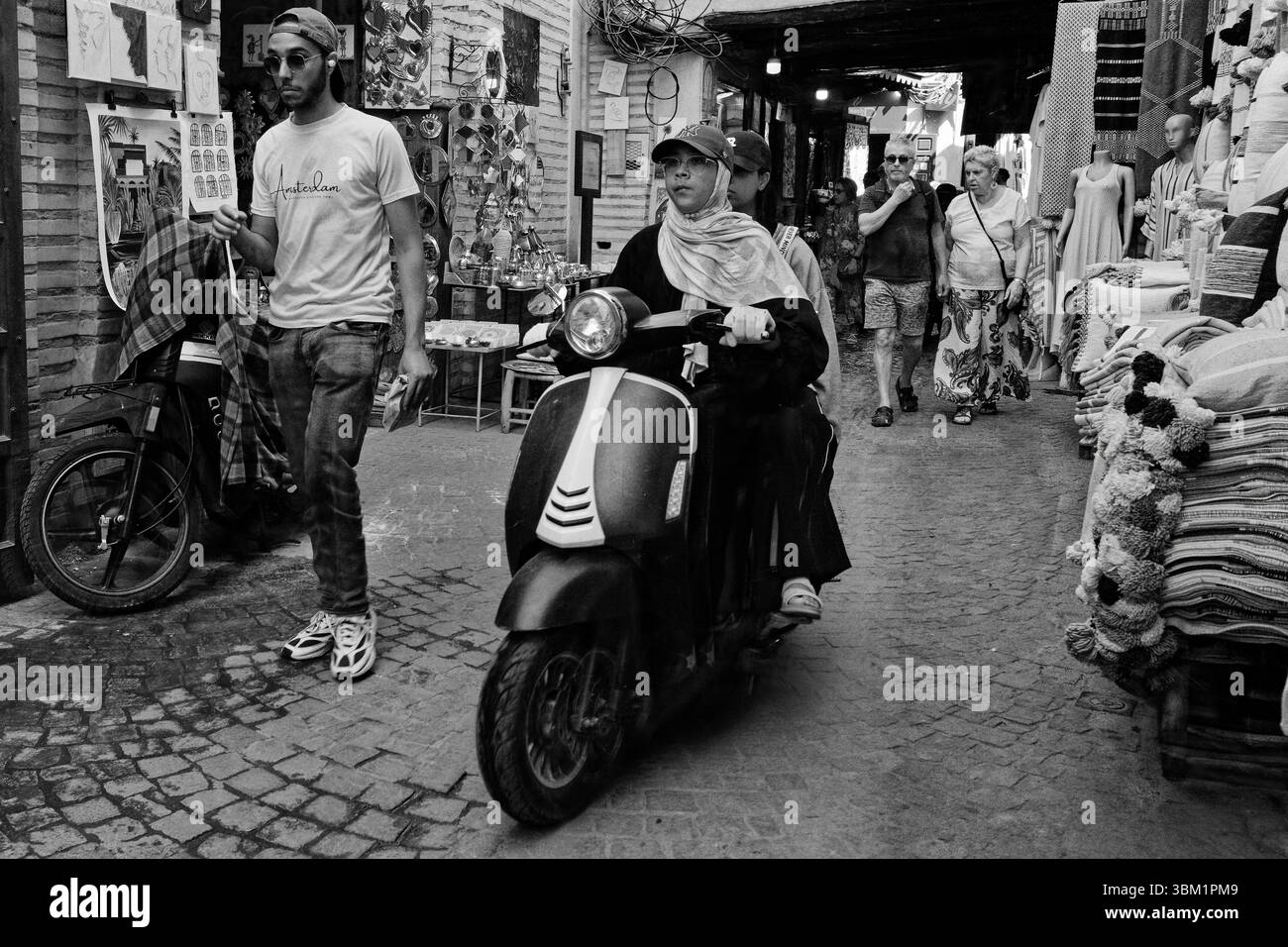 Eine Frau, die einen Roller durch eine enge Straße in einer Medina in Marokko fährt Stockfoto