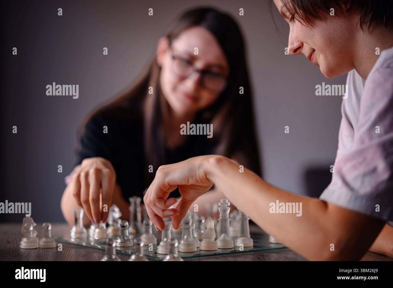 Zwei Freunde genießen eine Partie Schach, beide bewegen sich auf einem Glasschachbrett, teilen sich den Fokus und sind freundlich. Stockfoto