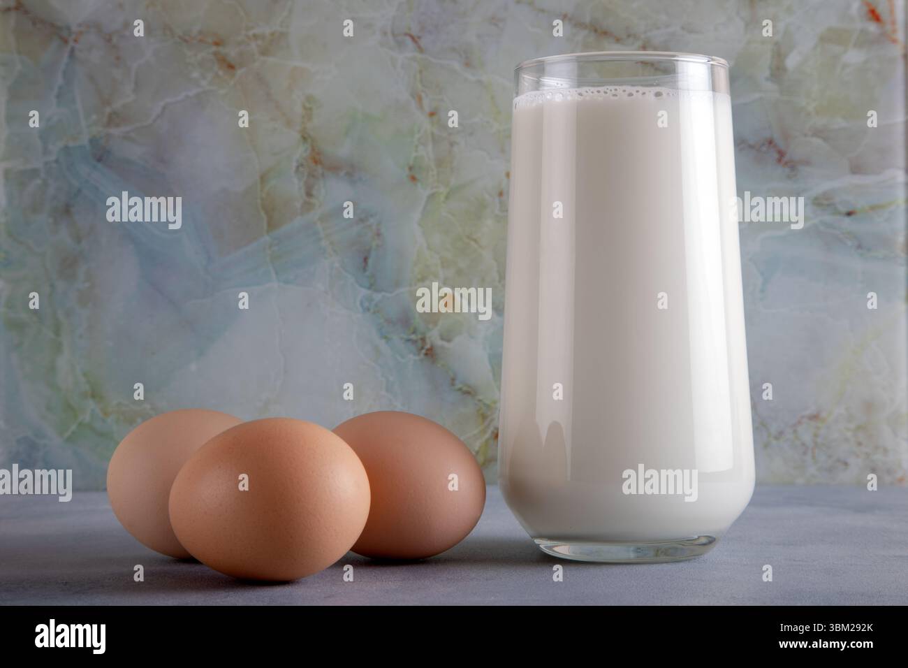 Ein Glas Milch und drei Eier auf dem blauen Tisch, Vorderansicht Stockfoto