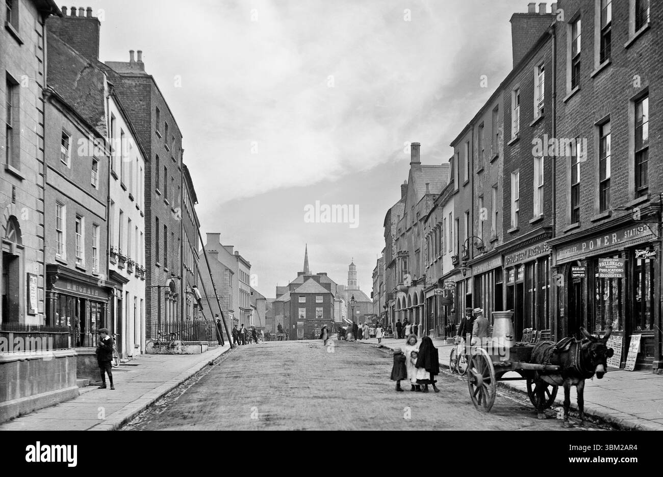Ein Foto aus dem späten 19. Jahrhundert von der Parliament Street in Kilkenny City, Irland. Ein Eselkarren, der eine Milchschleuder im Vordergrund transportiert, mit der fernen achteckigen Kuppel der Thostle im Hintergrund Stockfoto