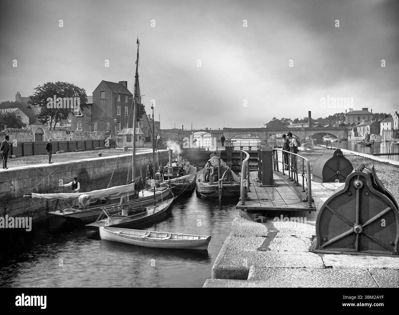 Eine Fotografie aus dem frühen 20. Jahrhundert von Lastkähnen und Yachten in der Schleuse am Westufer des Flusses Shannon in Athlone, County Roscommon, Irland. Sie befinden sich neben einem dazugehörigen Schleusenwärter/Hafenmeisterhaus, Teil der Shannon Navigation Works, die zwischen 1840-9 mit der Absicht stattfanden, den Shannon für erhöhten kommerziellen Verkehr und Handel zu öffnen. Stockfoto