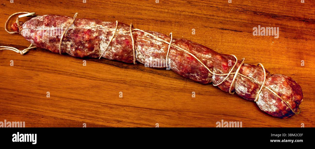 Ganze gepökelte Wurst, mit Garn verbunden, auf einem hölzernen Schneidebrett, die die traditionelle Kunst der Fleischkonservierung und die reichen Aromen von unterstreicht Stockfoto