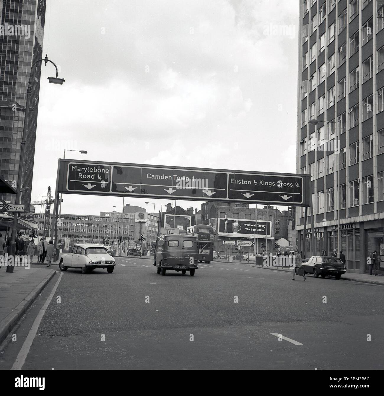 1960er Jahre, historisch, Euston Rd, Central London, England, Großbritannien, mit Overhead-Zielen und Richtungspfeilen. Auf der rechten Seite, in der Ferne, eine Werbetafel für Whitbread Trophy, die beste Bitter und auf Straßenniveau, unter einem modernen Turmblock, einer Zweigstelle der Midland Bank. Stockfoto