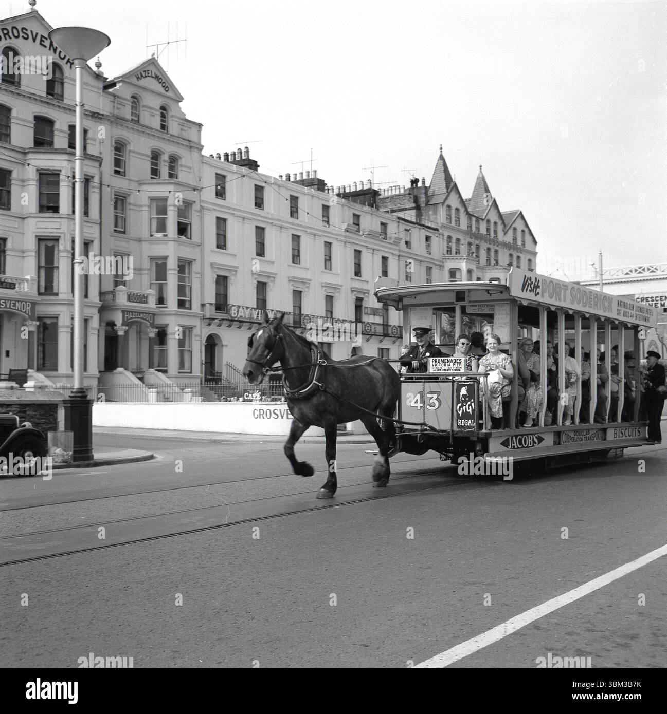 1950er Jahre, historisch, eine überdachte Pferdebahn, Nr. 43, auf einer Küstenstraße bei Douglas, Isle of man, Großbritannien. Schilder für die Promenaden Victoria Pier mit dem Schaffner, Fahrer und Passagieren an Bord. Auf der Seite der Straßenbahn heißt es in einer Werbetafel: Besuch von Port Soderick', einem Strand und Touristenziel in der Nähe von Douglas. Auch Werbung für Jacobs Kekse. Stockfoto
