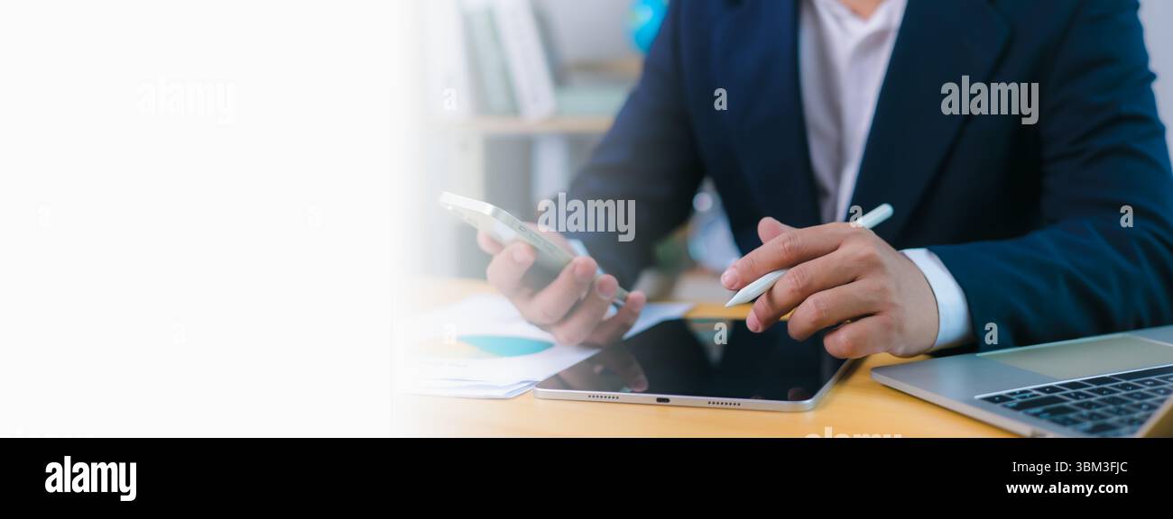 Geschäftsmann verwendet Telefon und Stift auf dem Tablet am Schreibtisch mit Laptop und Kopierraum , moderne Fernarbeit, digitale Produktivität, Technologieintegration, Stockfoto
