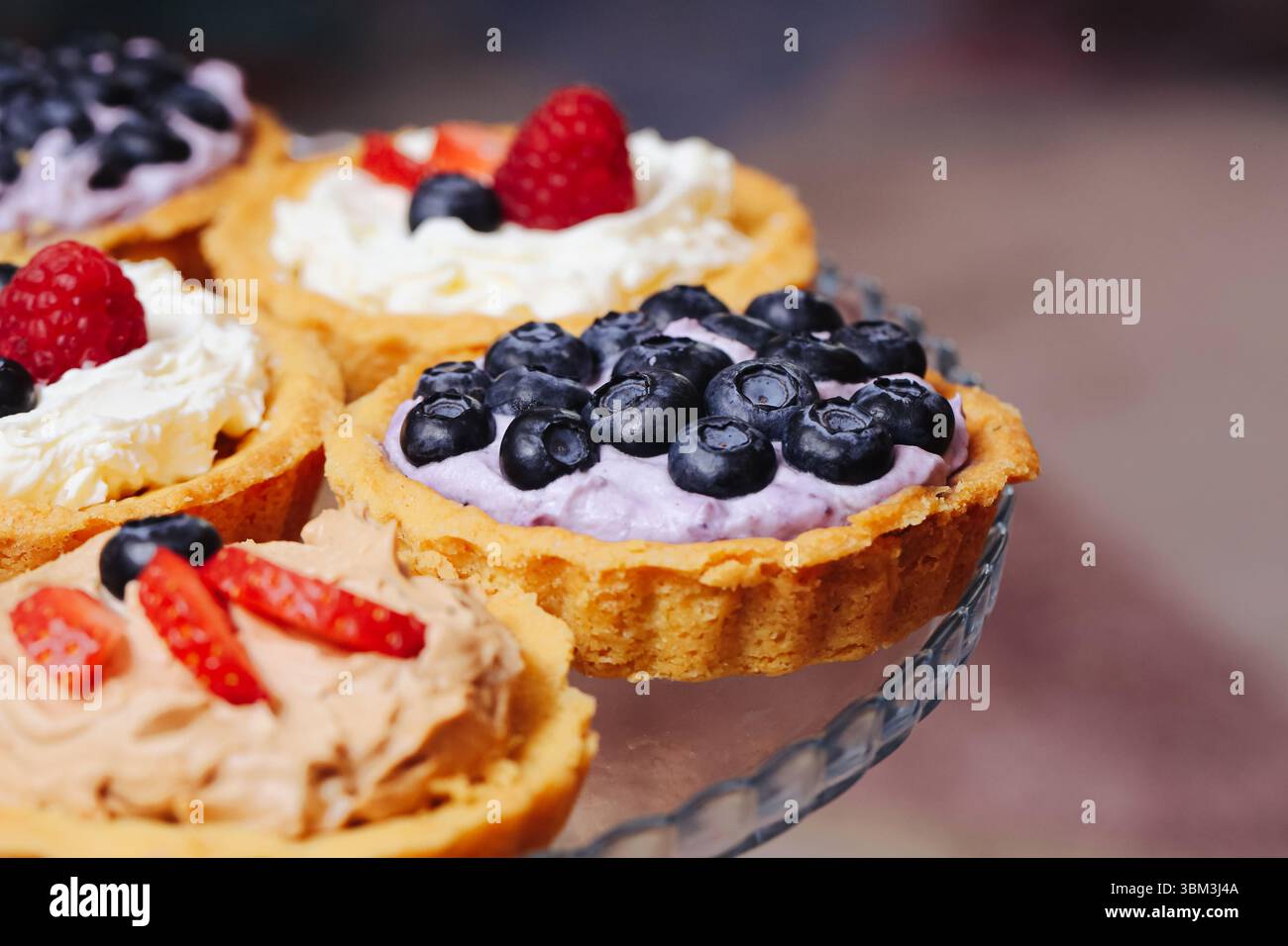 Süße Beerentörtchen aus nächster Nähe. Mini-Obstkuchen mit Sahne. Dessert mit Erdbeeren Heidelbeeren Himbeeren. Party-Food-Idee. Farbenfrohe Sommerspezialitäten Stockfoto