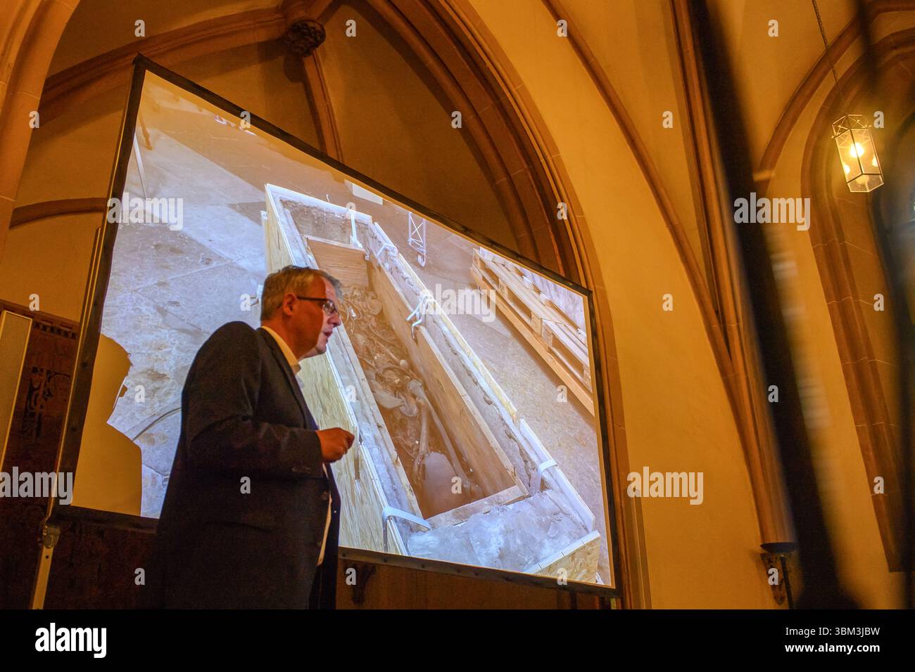 24. Juni 2025, Sachsen-Anhalt, Magdeburg: Donat Wehner (l) vom Landesamt für Denkmalpflege und Archäologie Sachsen-Anhalt erklärt Medienvertretern in der Sakristei des Magdeburger Doms mit Hilfe einer Live-Videoübertragung aus dem Inneren des Gehäuses um das Grab Ottos des Großen den Schaden in der Holzkiste, in der Knochen zu sehen sind. Seit Januar führen das Landesamt für Denkmalpflege und Archäologie und die Kulturstiftung Sachsen-Anhalt Untersuchungen zur Erhaltung des Denkmals durch. Die Resu Stockfoto