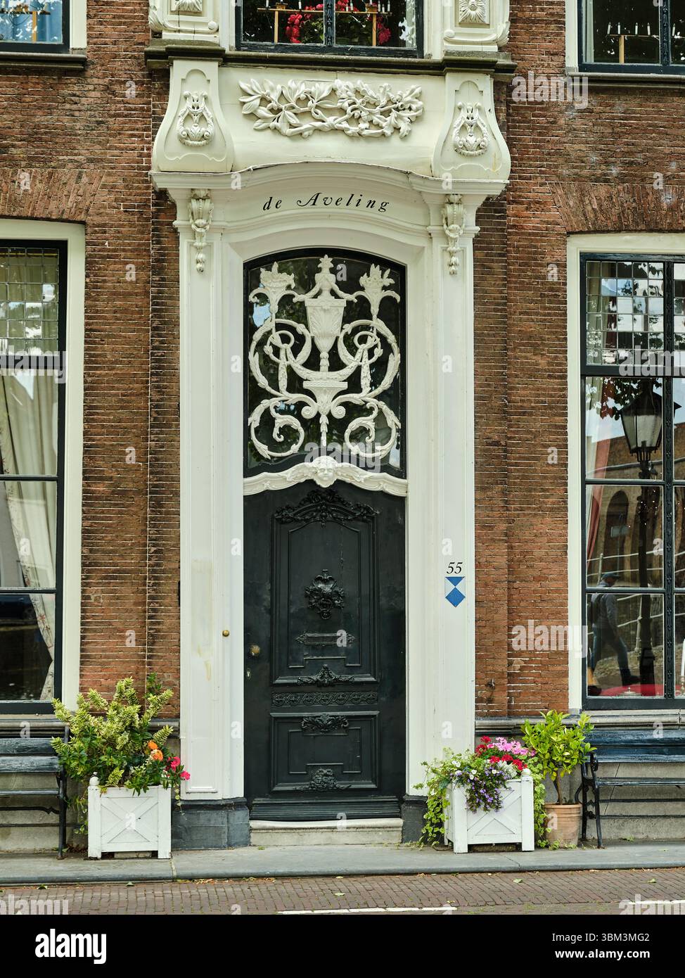 26. Mai 2025 - Zierikzee-Niederlande: Historisches Stadthaus de Aveling mit verzierten schwarzen Türen, großen Fenstern und bunten Blumenkästen vor einem Stockfoto