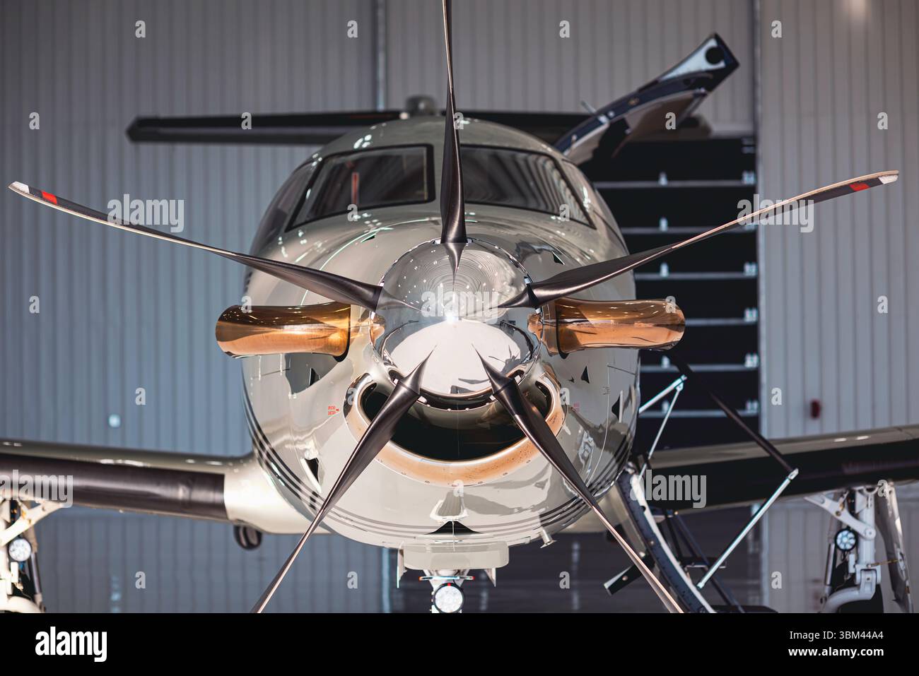 Symmetrische Vorderansicht eines privaten Turboprop-Flugzeugs in einem Hangar mit polierten Spinner, Propellerblättern und Auspuffkomponenten. Stockfoto