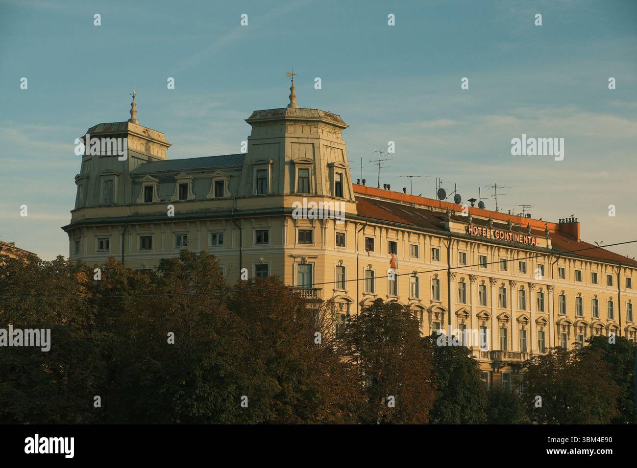 Die elegante Fassade des historischen Hotels Continental lässt sich in warmer Abendsonne erstrahlen, die cremigen Töne und kunstvollen architektonischen Details leuchten sanft. Stockfoto
