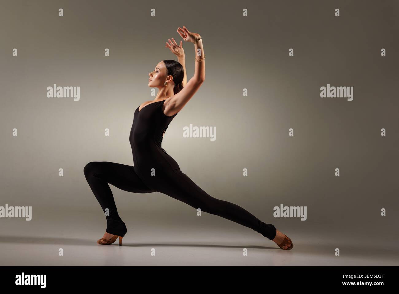 Sportliche Tänzerin in schwarzem Body trifft im Studio eine kräftige lateinische Tanzposition, perfekt für Salsa, Tango und Bachata. Stockfoto
