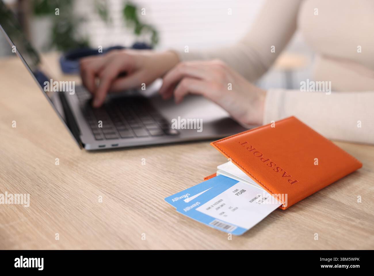 Frau mit Laptop an Holztisch mit Reisepass und Flugtickets drinnen, Nahaufnahme Stockfoto