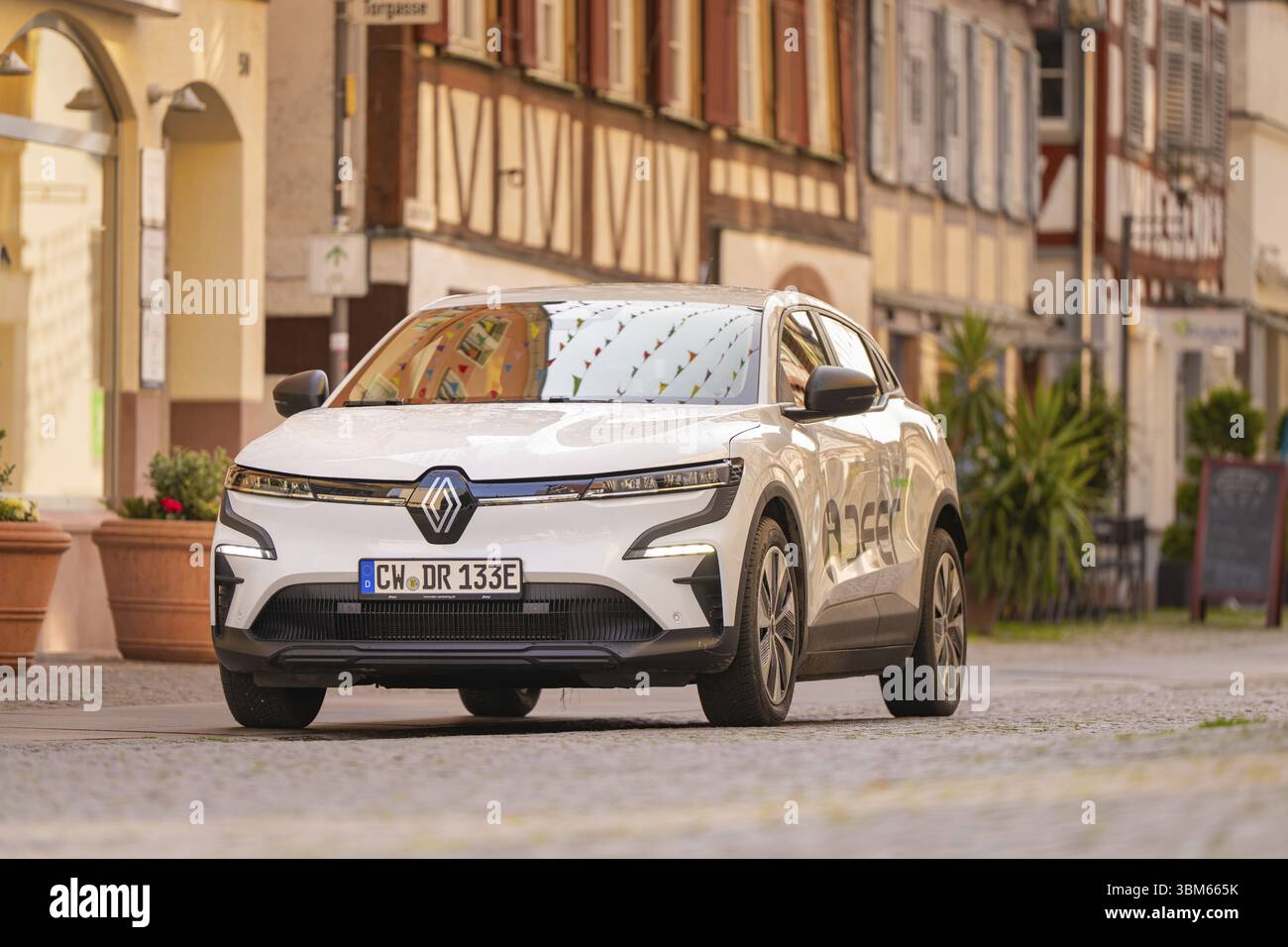 Ein Auto fährt entlang einer Kopfsteinpflasterstraße, gesäumt von traditionellen Fachwerkhäusern, bei hellem Sonnenlicht, Hirsch E, Carsharing, Elektroauto, Calw, Schwarz F Stockfoto