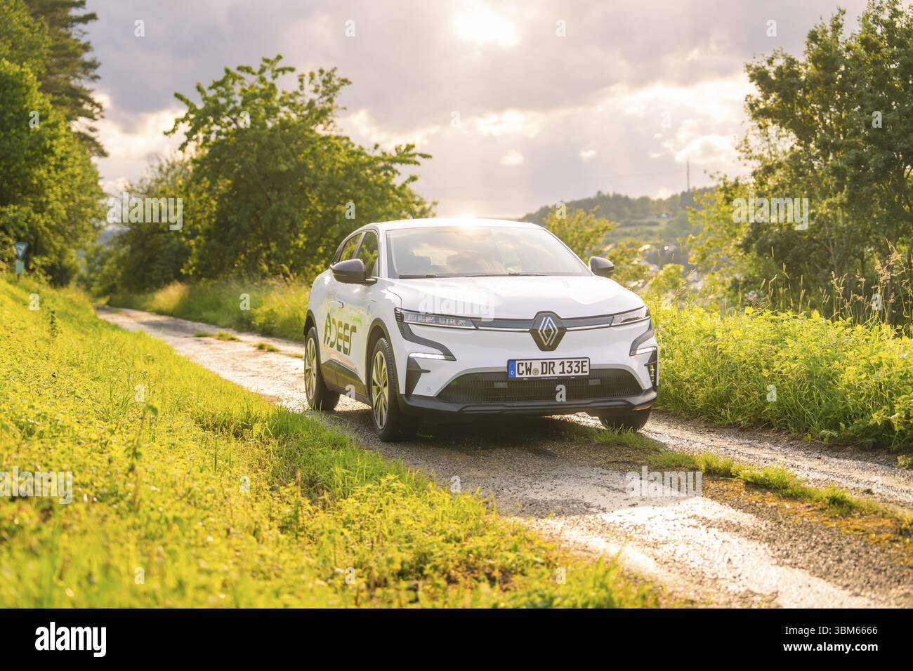 Ein weißes Elektroauto fährt entlang einer ländlichen Schotterstraße, umgeben von Bäumen im Sonnenlicht, Hirsch E, Carsharing, Elektroauto, Calw, Schwarzwald Stockfoto