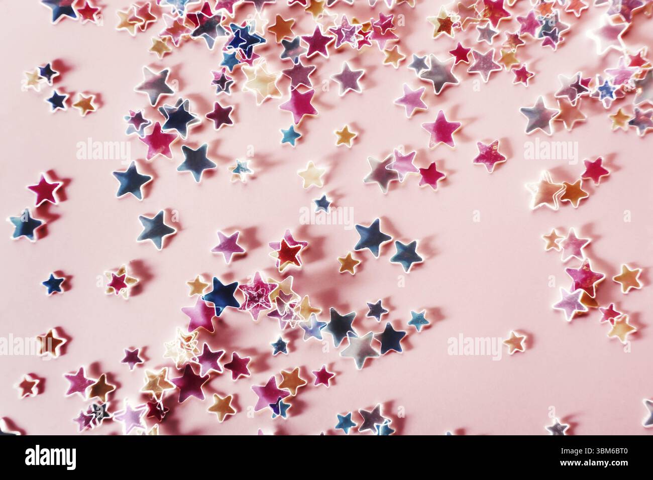 Mehrfarbige holographische Sterne Glitter Konfetti auf rosa Hintergrund. Festliche Kulisse, selektiver Fokus Stockfoto