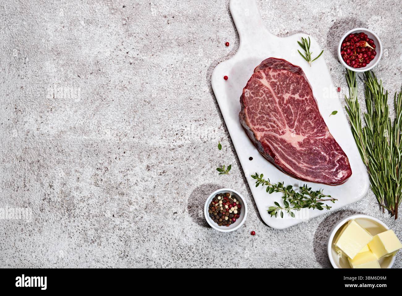 Frisches marmoriertes Rinderrib Eye Steak und Gewürze auf grauem Steinhintergrund, trendige Schatten Stockfoto