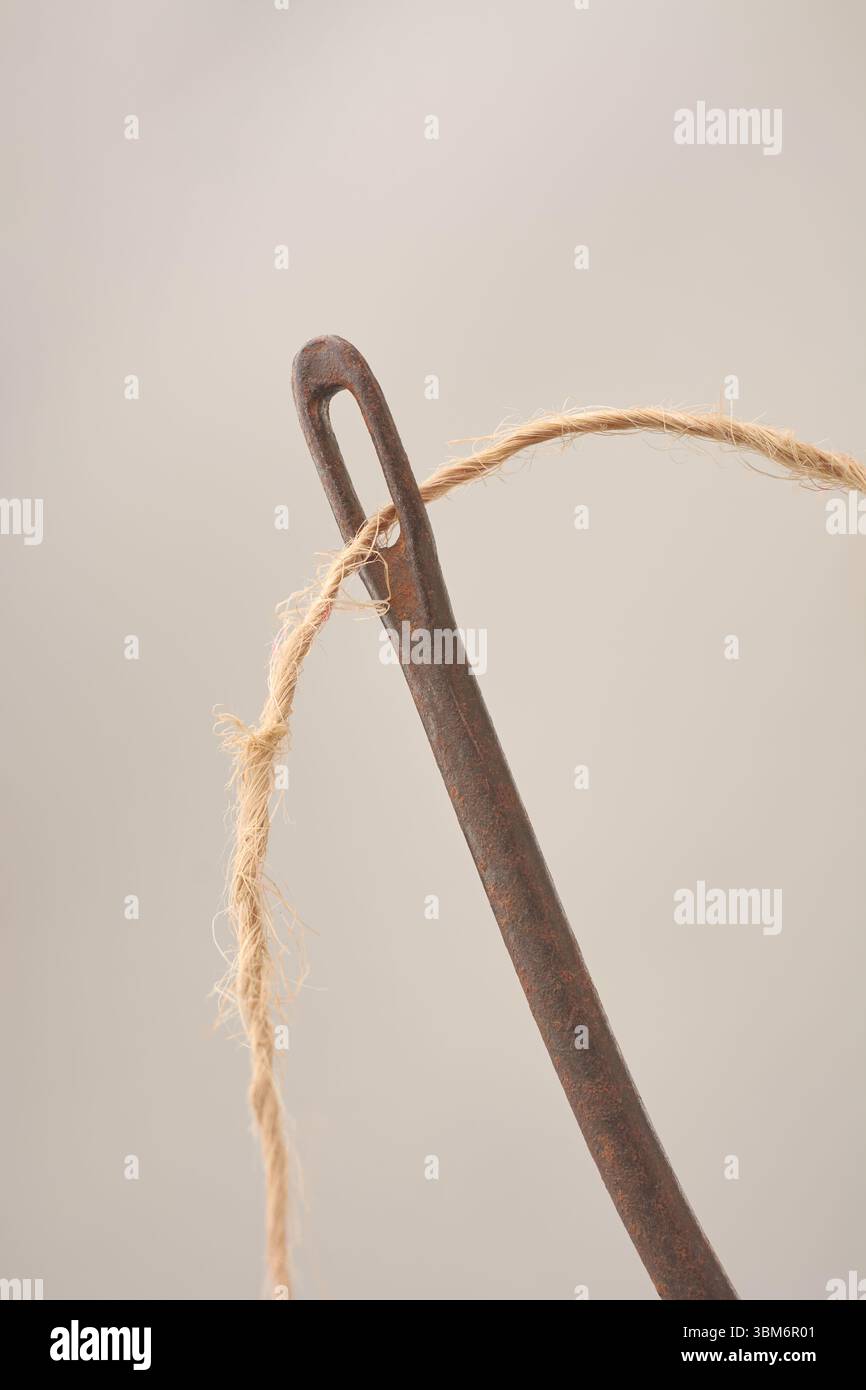 Nahaufnahme von grobem Kokosnussfaden durch Auge alter rostiger Sacknadel isolierter neutraler grauer Hintergrund, Natur- und Industriematerialkonzept Stockfoto