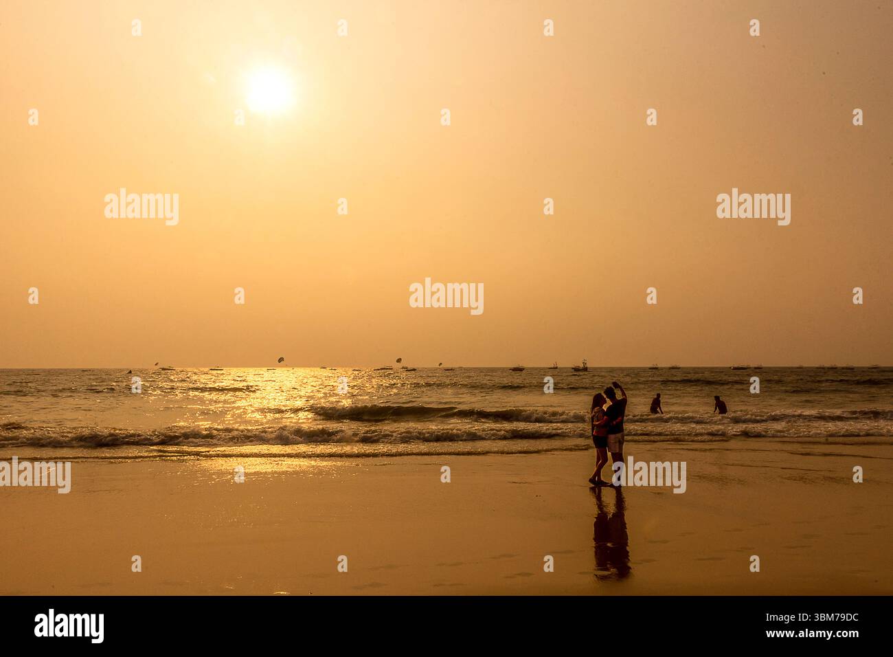 Ein romantischer goldener Sonnenuntergang lässt den Himmel am Baga Beach in Goa, Indien, in Brand, während ein Paar ein freudiges Selfie an der Küste festnimmt. Stockfoto