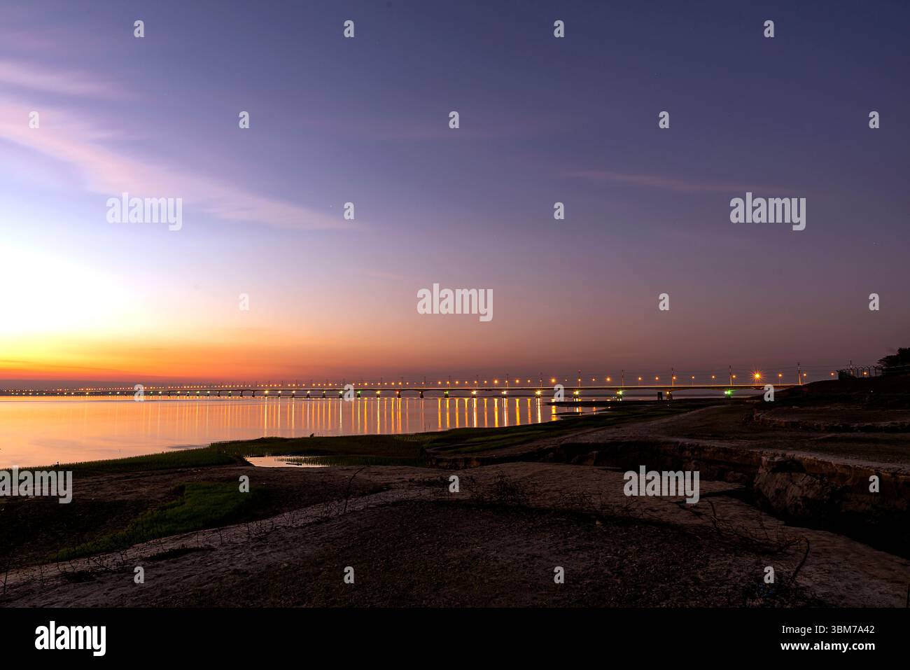 Ein faszinierender goldener Sonnenuntergang über dem Jamuna River in Tangail, Bangladesch, mit der berühmten Jamuna Bridge, die vor bunten Lichtern leuchtet. Stockfoto