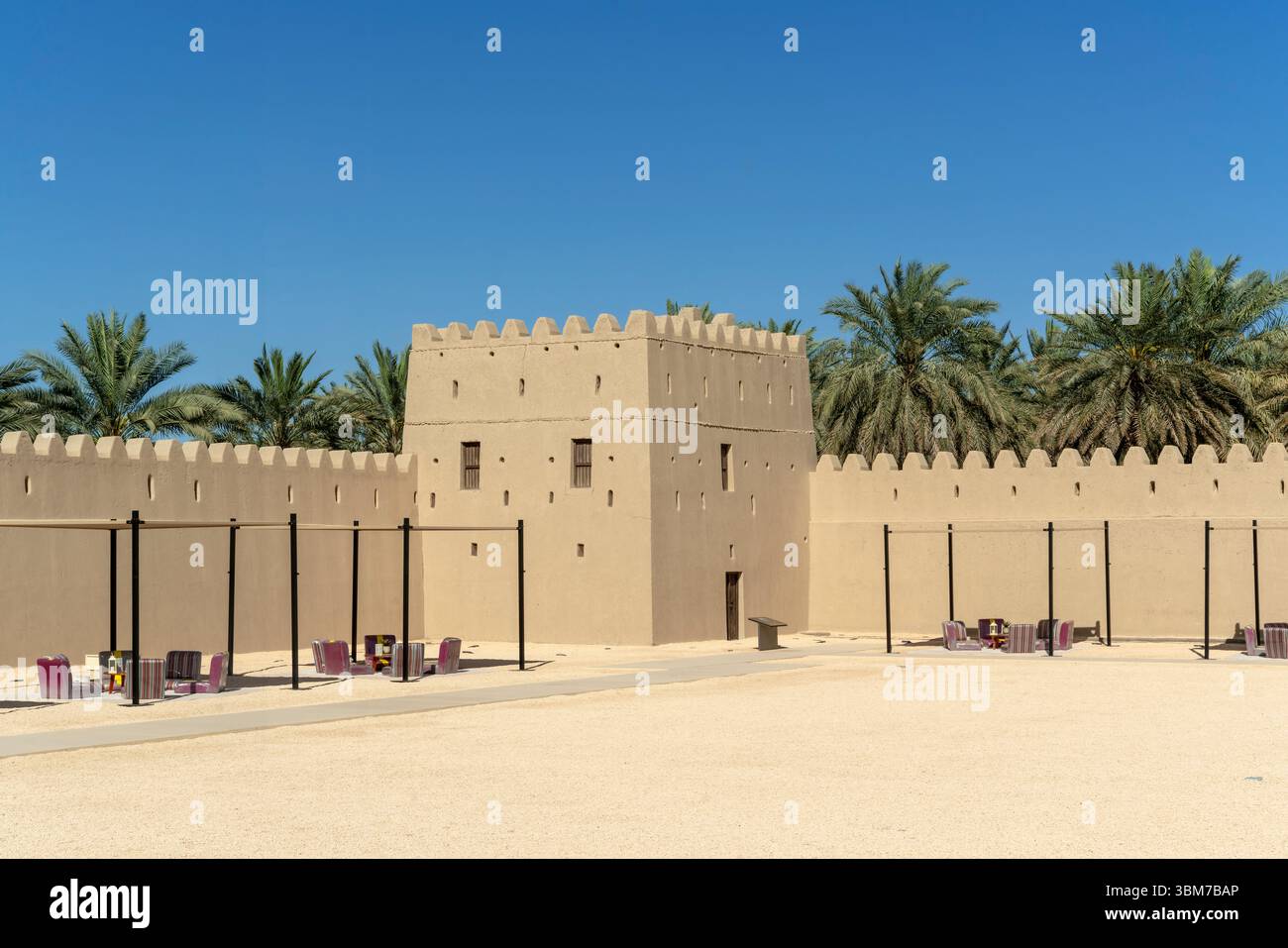 Großer quadratischer Festungsturm mit schmalen Schlitzfenstern erhebt sich über einer Lehmziegelmauer bei Qasr Al Muwaiji in Al Ain Vereinigte Arabische Emirate. Stockfoto