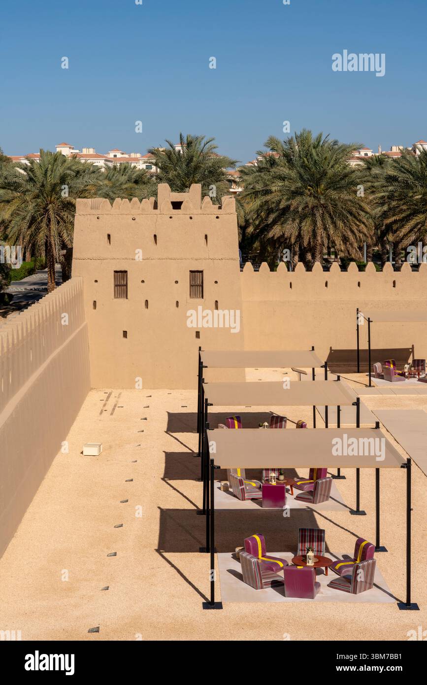 Innenhof mit Palmen und Lehmziegelmauern, umgeben von zinnenverzierten Türmen im Qasr Al Muwaiji in Al Ain Vereinigte Arabische Emirate. Stockfoto