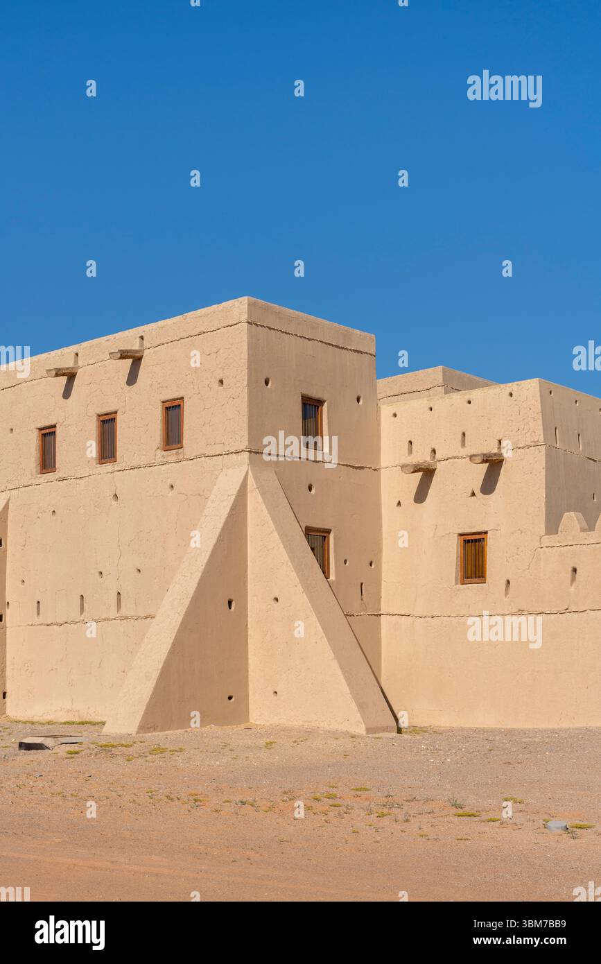 Weitläufiger, sandiger Innenhof mit schattigen Sitzgelegenheiten und von Palmen gesäumten Festungsmauern im Qasr Al Muwaiji in Al Ain Vereinigte Arabische Emirate. Stockfoto