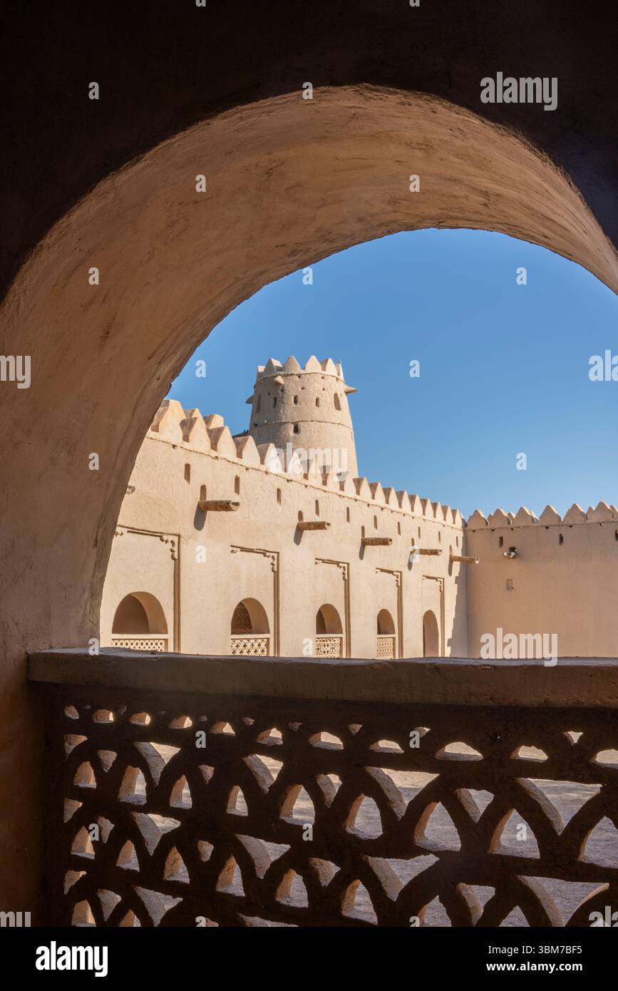 Eine große bogenförmige Öffnung umrahmt den Blick auf eine historische Festung mit zinnenbesetzten Mauern und Türmen am Al Jahili Fort in Al Ain Vereinigte Arabische Emirate. Stockfoto