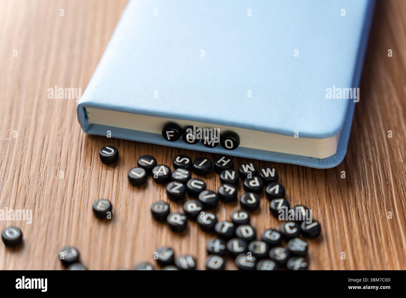 Buchstabenperlen mit der Schreibweise „FOMO“ mit mehr verstreuten Perlen auf einem Holztisch. Angst vor dem Verpassen, soziale Angst und psychische Gesundheitskonzepte. Stockfoto