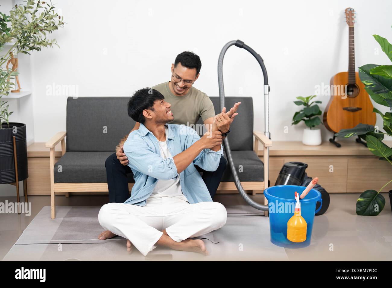 Fröhliches Reinigungserlebnis. Freunde, die ein Lächeln teilen, während sie in ihrem gemütlichen Zuhause saugen. Stockfoto