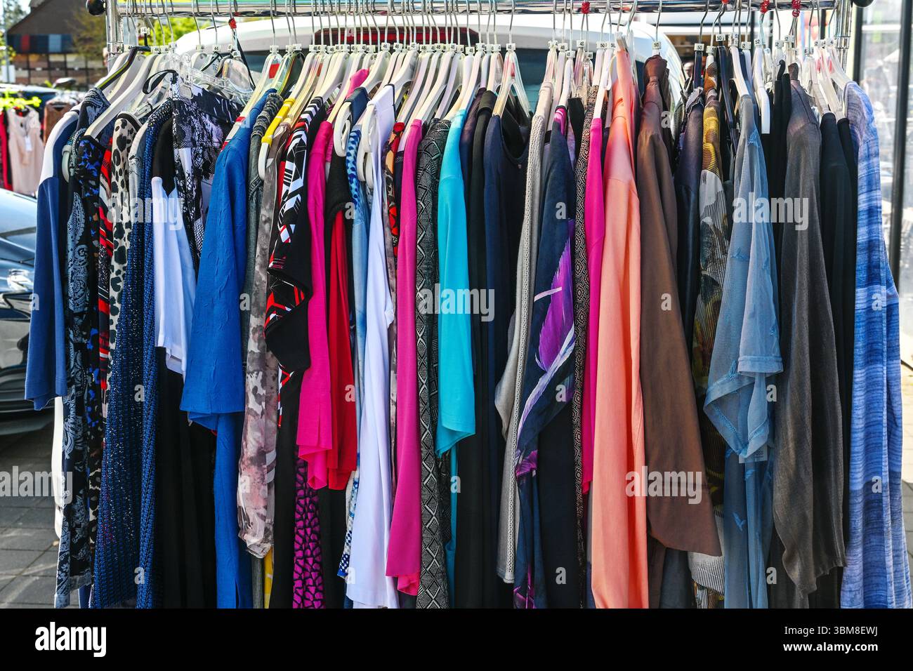 Farbenfrohe gebrauchte Kleidung, die an einem Regal zum Verkauf auf einem Flohmarkt an einem sonnigen Tag hängt, ausgewählter Fokus, enge Schärfentiefe Stockfoto
