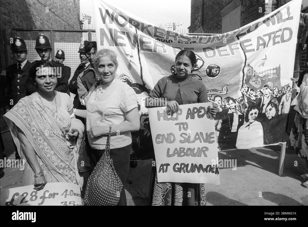 Frau Jayaben Desai links mit einem Banner, auf dem 28-00 Pfund für 40 Stunden steht. Ein Unterstützer aus Südafrika (Mitte). Yasu Patel mit dem Banner „Helft Apex, Sklavenarbeit in Grunwick zu beenden“. Grunwick Streik und Arbeitskampf. Willesden, London, England, 1977 1970er Jahre Großbritannien HOMER SYKES Stockfoto