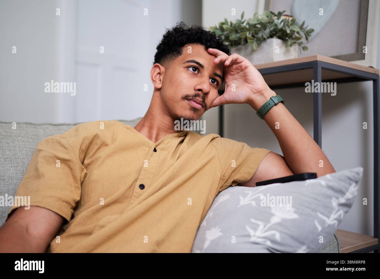 Mann, der sich zu Hause auf einer Couch entspannt, in einer nachdenklichen Pose mit neutralen Tönen Stockfoto