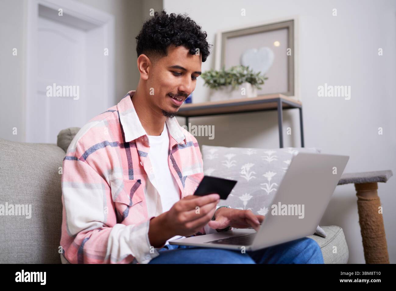 Junge Erwachsene kaufen online zu Hause mit Laptop und Karte Stockfoto