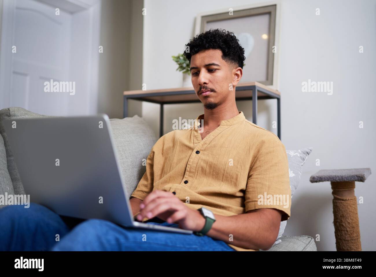 Mann, der auf einem Sofa sitzt und einen Laptop in einer komfortablen Wohnumgebung benutzt Stockfoto