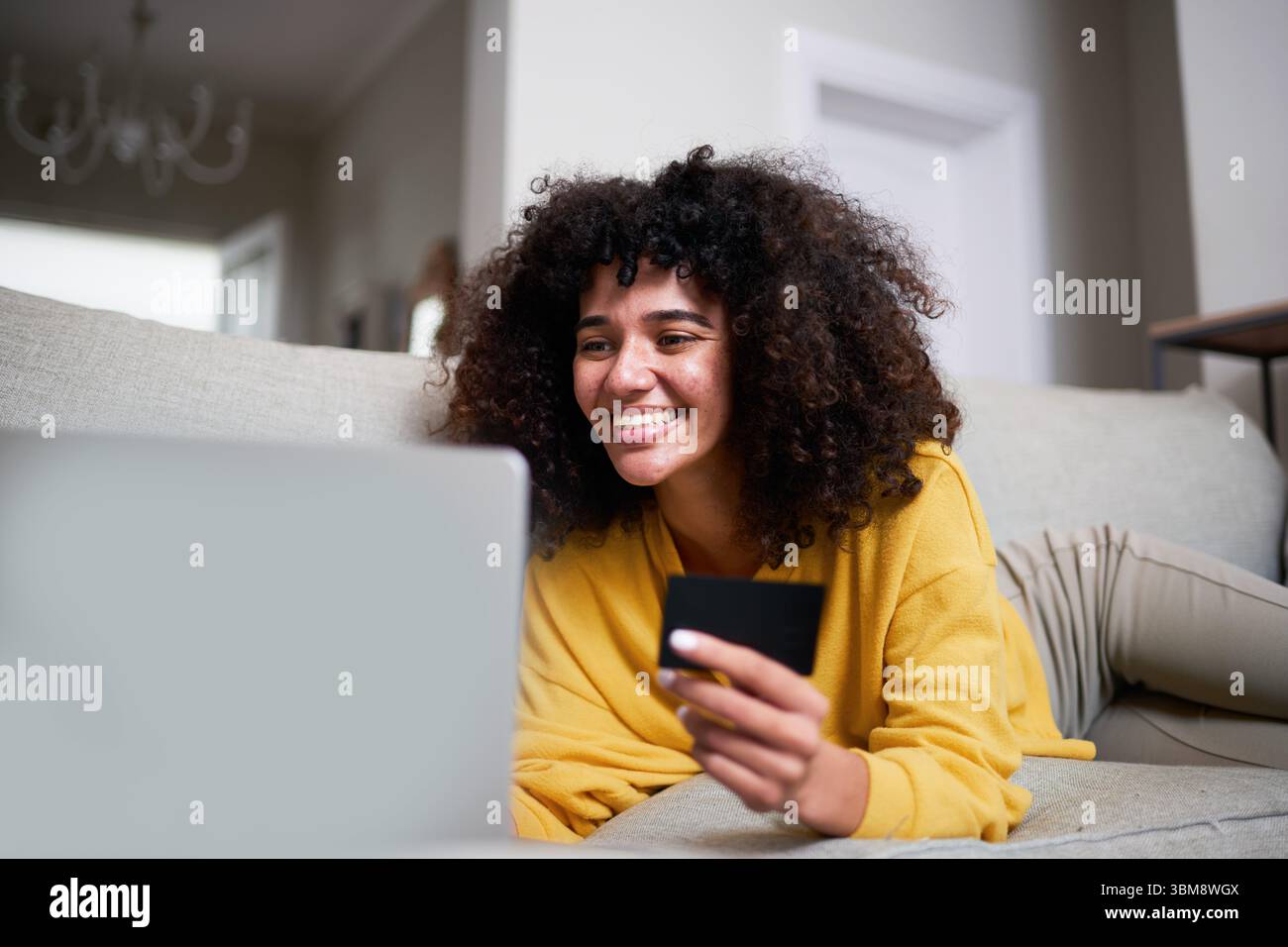 Junge Frau, die von zu Hause aus mit Laptop und Kreditkarte online einkaufen Stockfoto