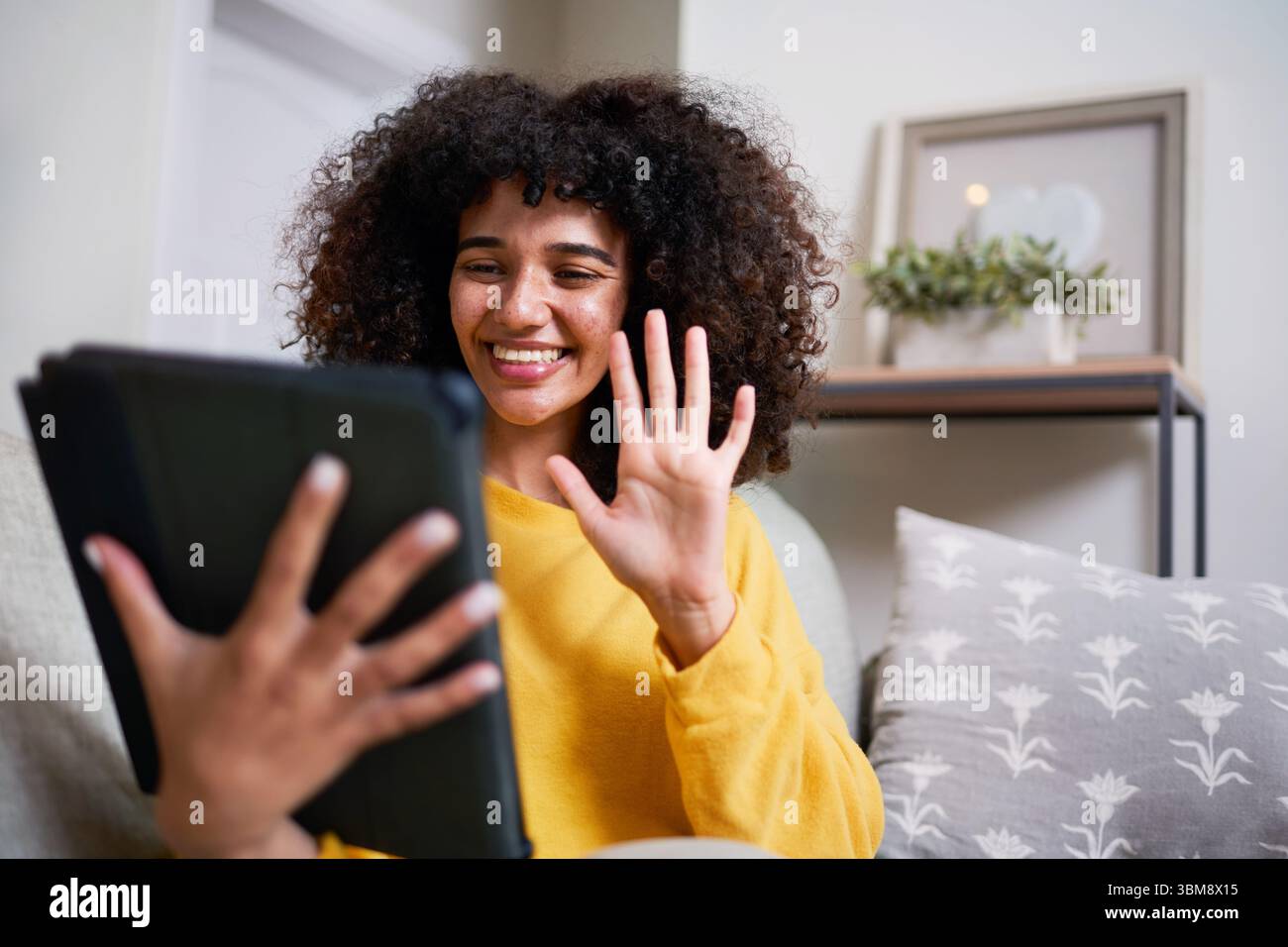 Lächelnde Frau im Videoanruf mit Tablet, während sie im gemütlichen Wohnzimmer sitzt Stockfoto