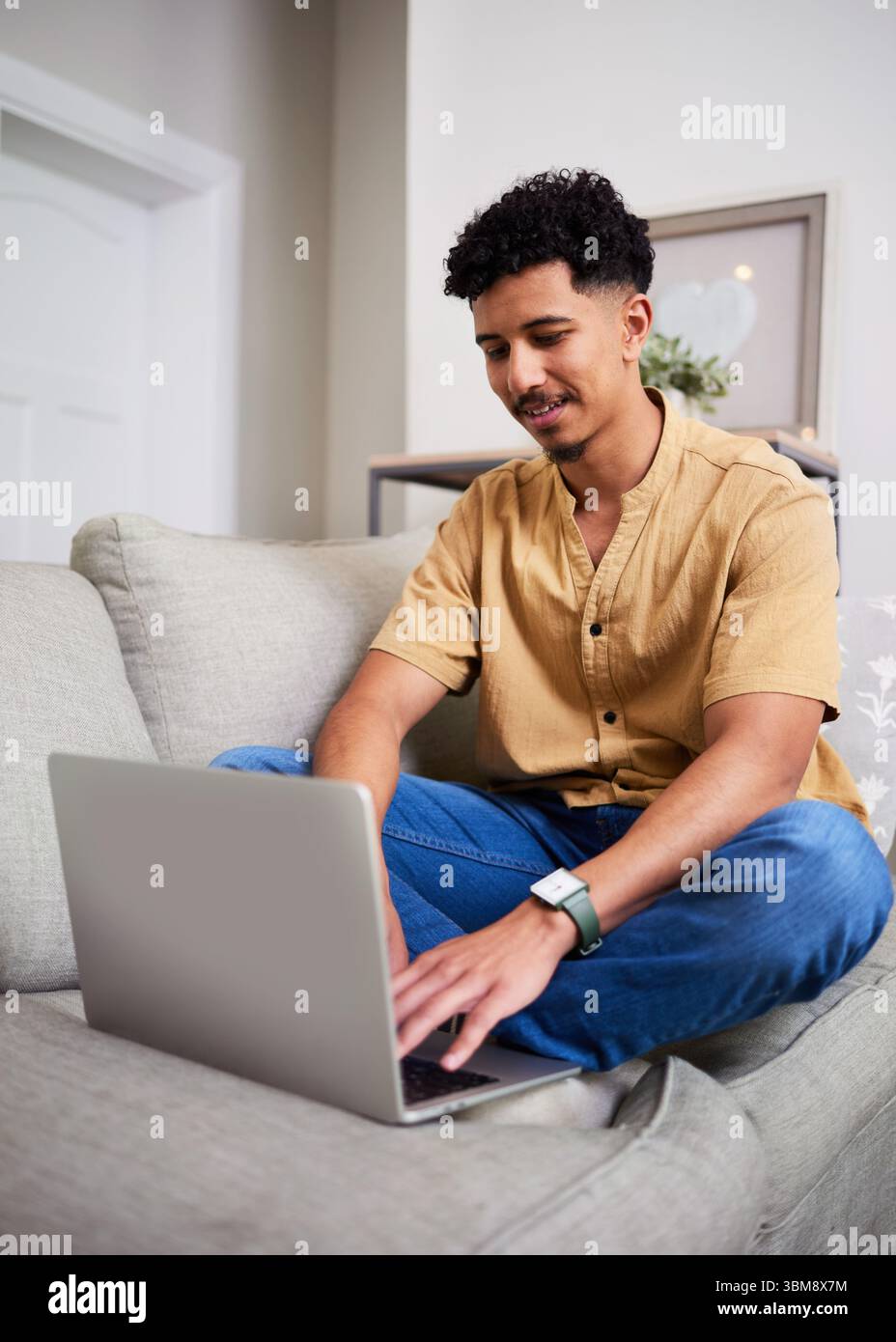 Mann sitzt bequem auf der Couch mit Laptop in einer modernen, hellen Wohnumgebung Stockfoto