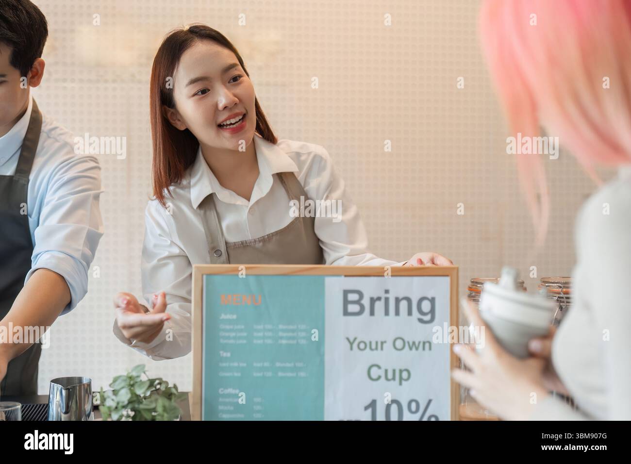 Nachhaltigkeit und Kundenbindung. Ein Barista erklärt, welche Vorteile es hat, einem Gast in einem trendigen Café einen persönlichen Becher mitzubringen. Stockfoto