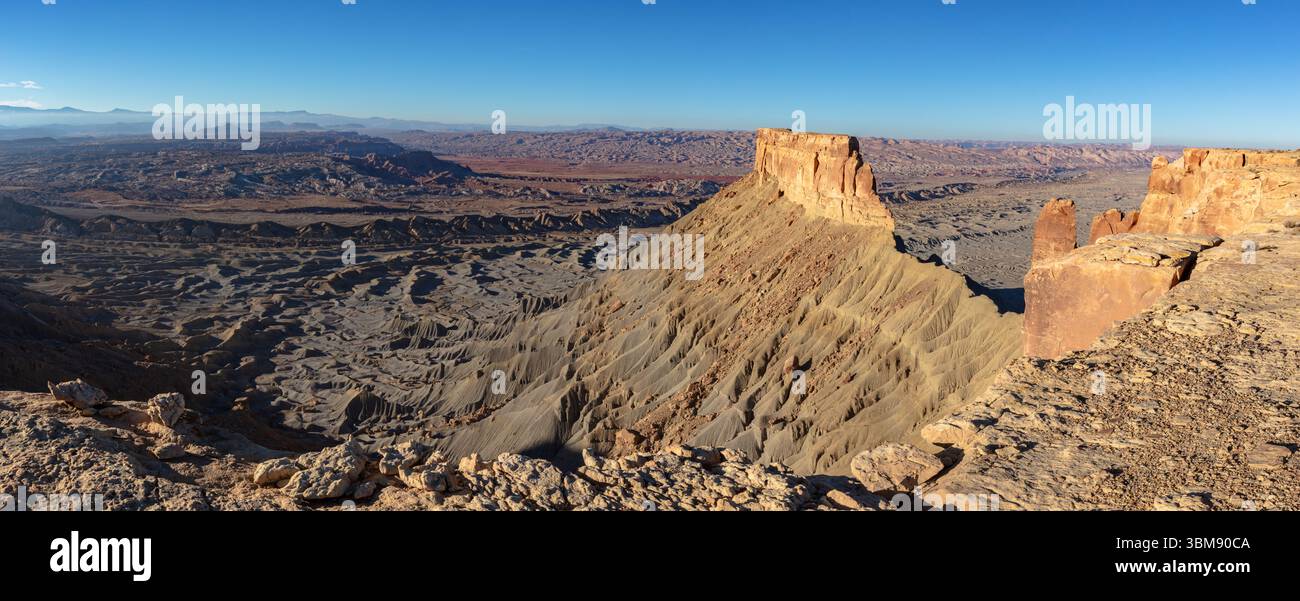 Die Klippen von North Caineville Mesa erheben sich über das North Caineville Reef und die zerklüfteten, farbenfrohen Utah Badlands bei Sonnenuntergang an einem Tag mit Blauvögeln. Stockfoto