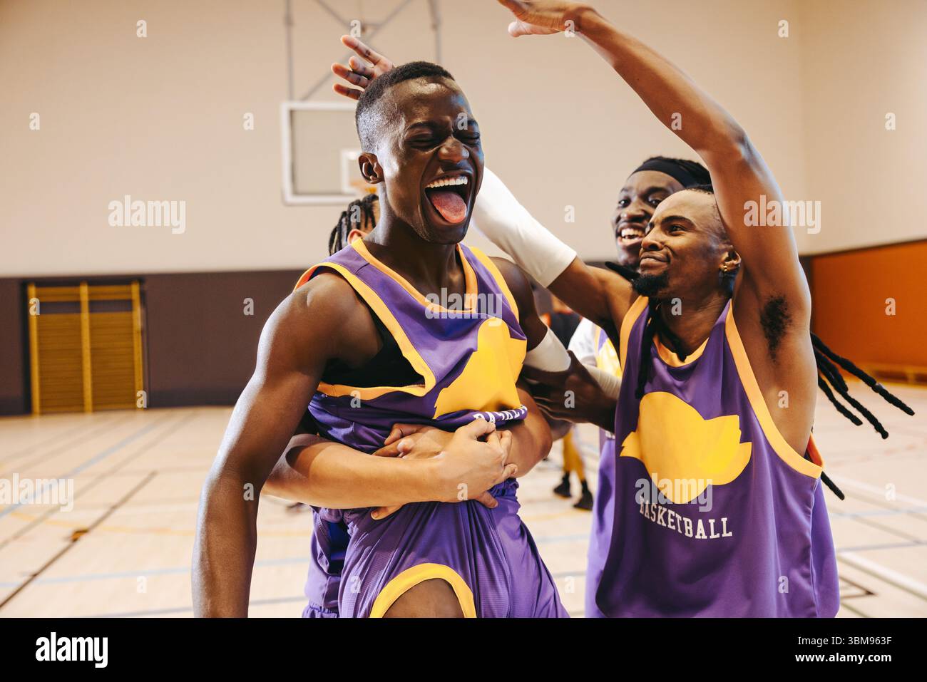 Ein junges männliches Basketballteam feiert beim letzten Pfiff, überwältigt von Stolz und Erleichterung nach einem hart umkämpften Spiel. Stockfoto