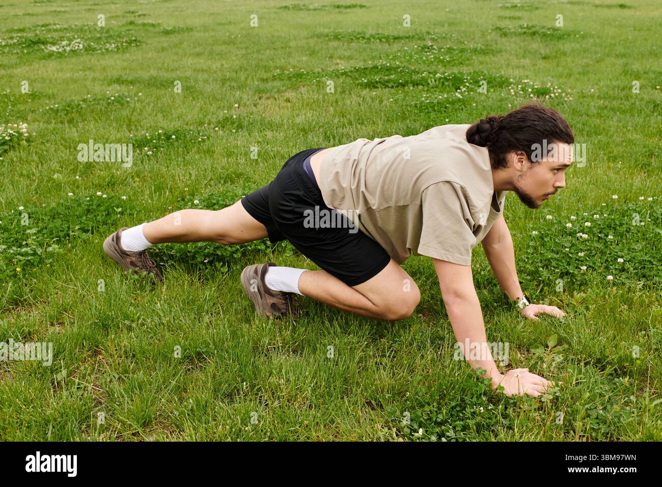 Junger Mann mit Bart trainiert intensiv auf grasbewachsenem Boden und demonstriert Agilität und Kraft. Stockfoto