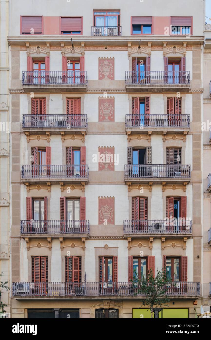 Historische Fassade Des Barcelona-Gebäudes Mit Roten Fensterläden Und Verzierten Details. Traditionelle Architektur, städtisches Leben, europäische Stadt, dekorative Elemente, c Stockfoto
