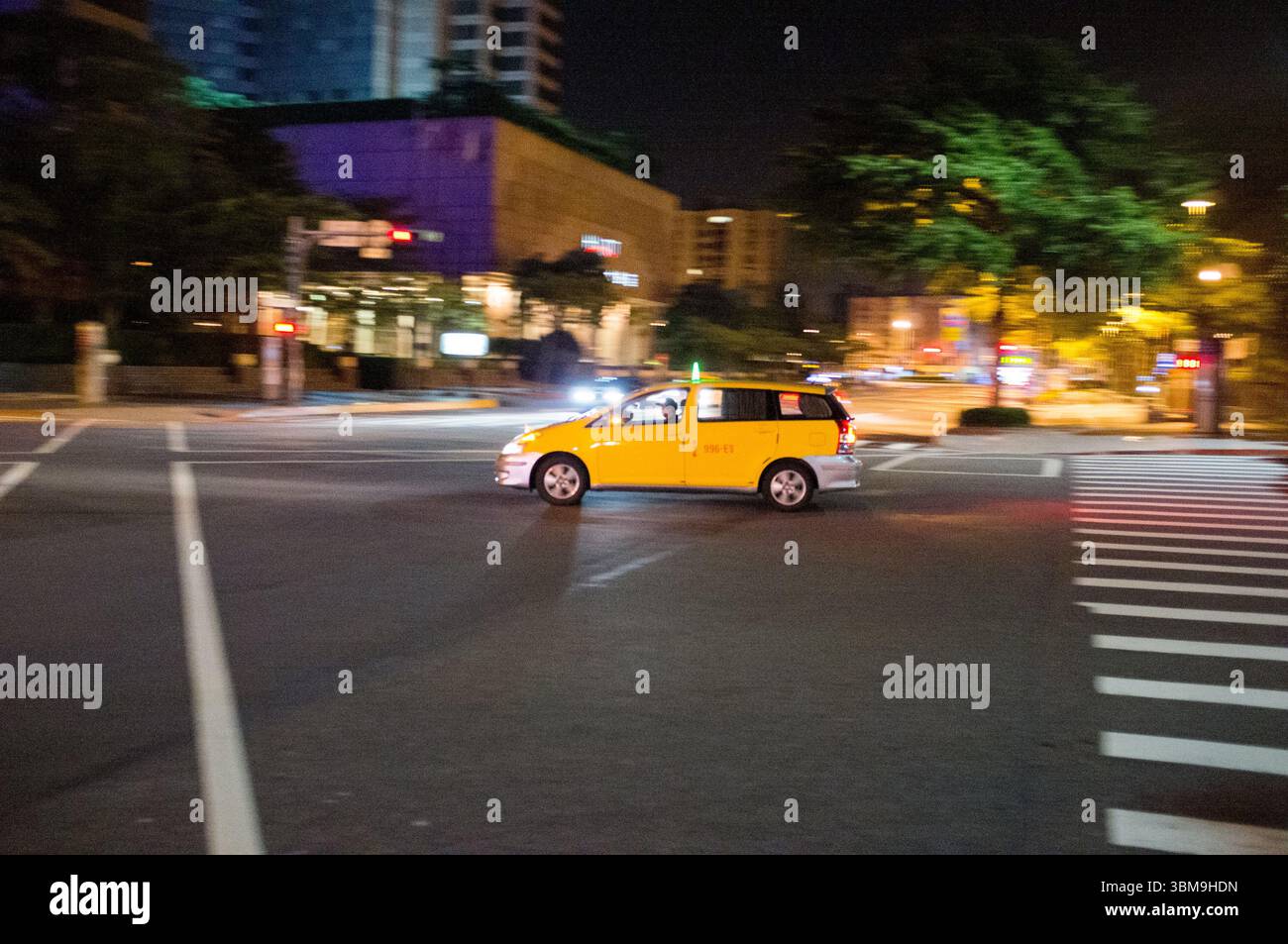 Bewegungsunschärfe eines gelben Fahrerhauses, das durch eine Nachtstraße in Taipei fährt und die pulsierende urbane Atmosphäre und das dynamische Stadtleben einfängt. Stockfoto
