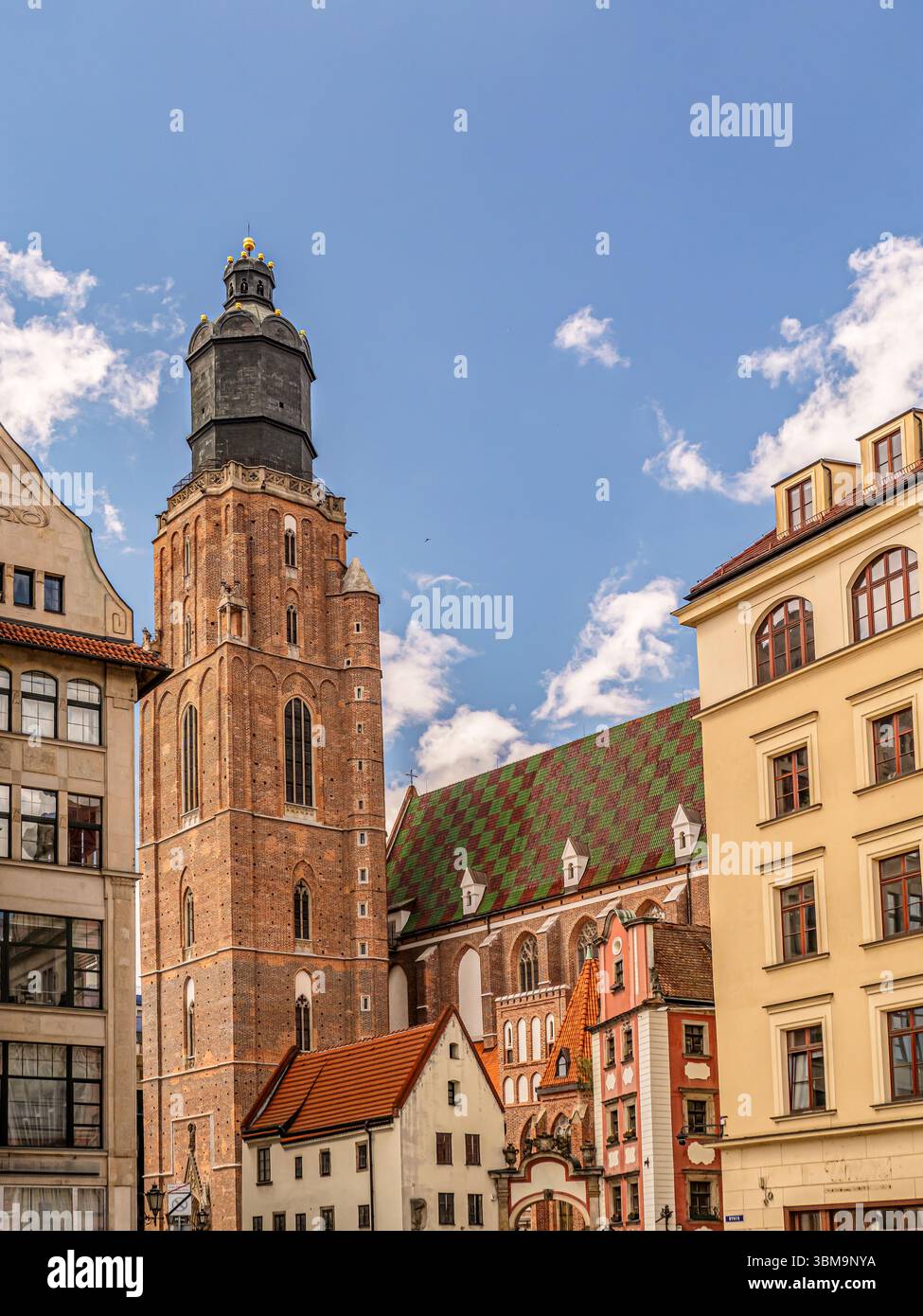 Ein beeindruckender Blick auf einen historischen Backsteinturm der St. Elisabeth Kirche, umgeben von lebhaften Dächern und bezaubernder Architektur unter einem hellen, wolkengepunkteten B Stockfoto