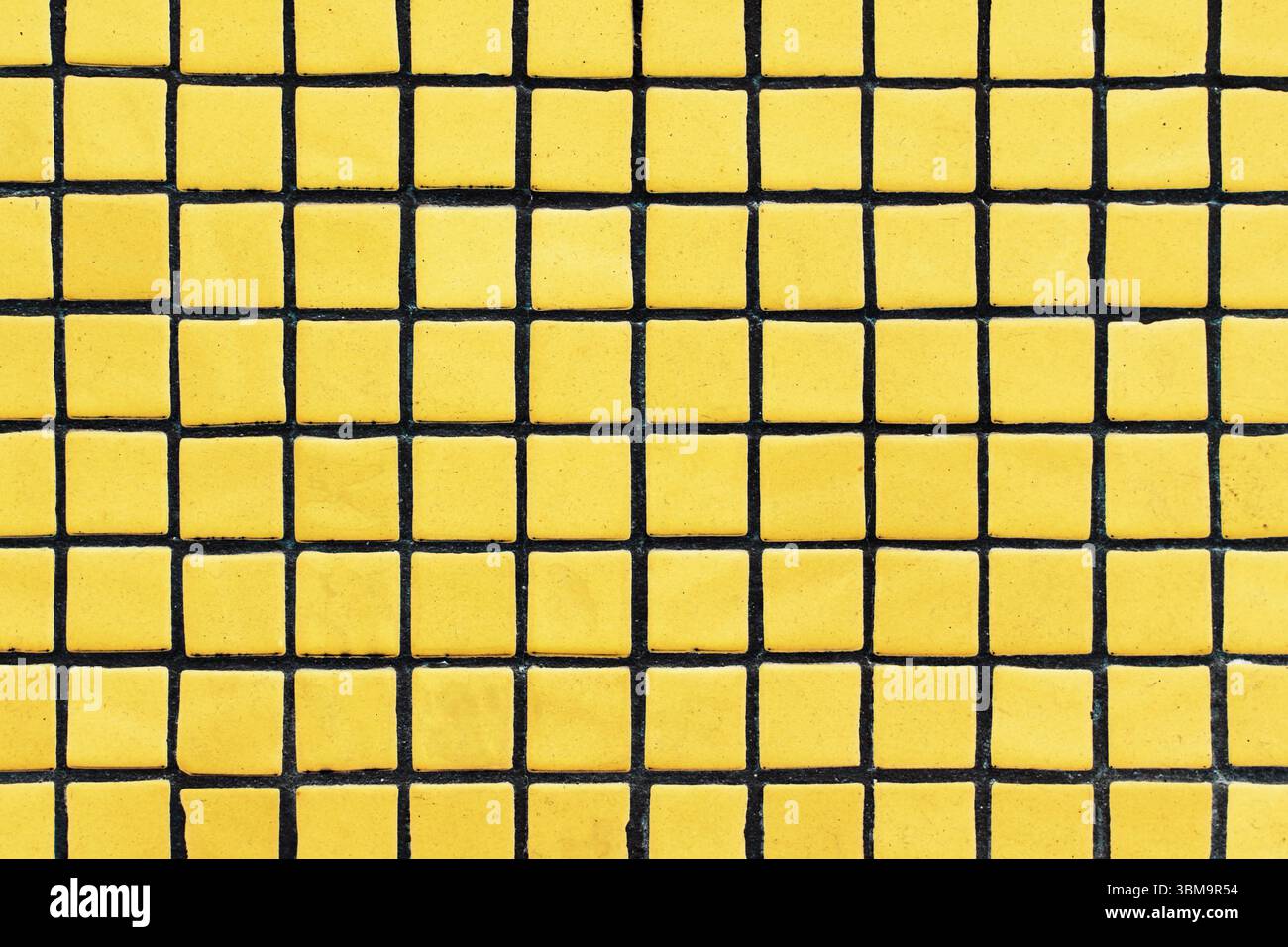 Gelbe Fliesen mit schwarzem Raster. Geometrisches Muster mit Kontrastfarben. Abstrakter Hintergrund von Quadraten. Städtisches Wanddesign. Moderne dekorative Oberfläche. Stockfoto