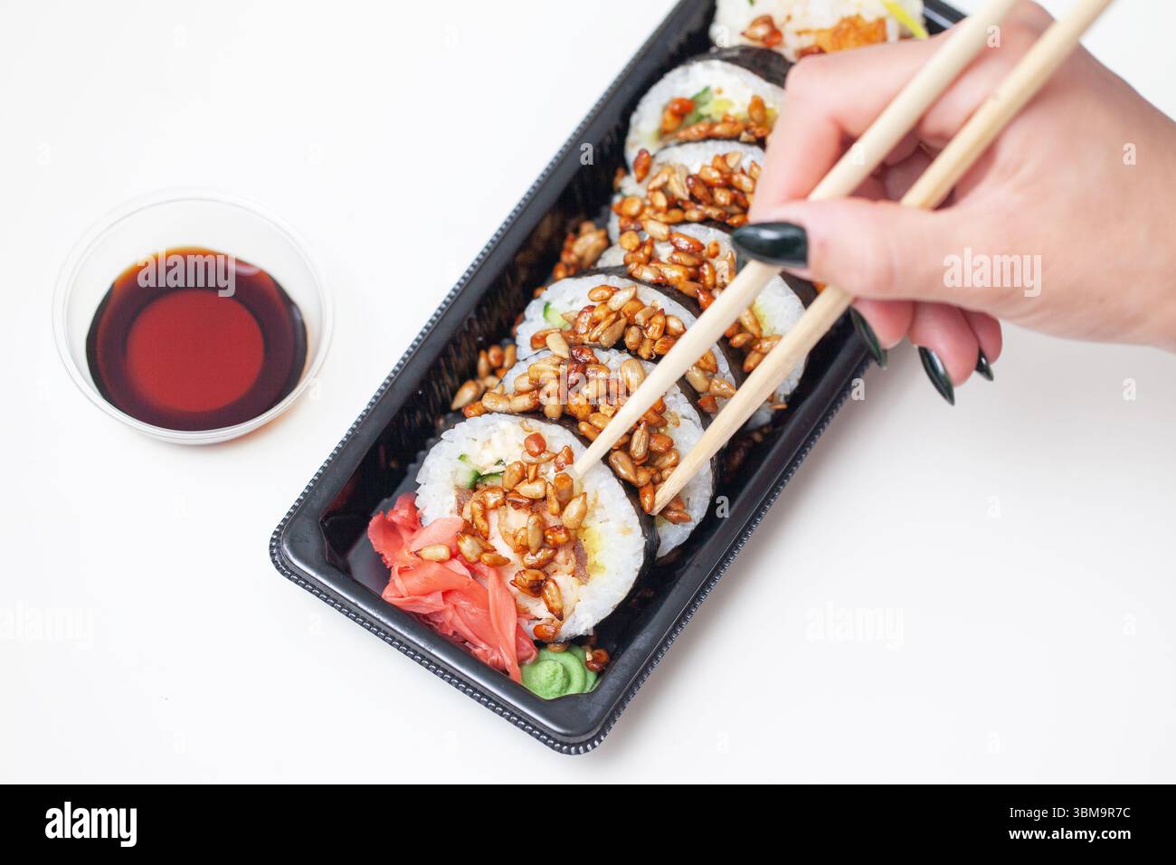 Frau mit Sushi-Rolle. Stäbchen für traditionelle Reisrollen. Asiatisches Mittagessen mit Sojasauce in einer kleinen Schüssel. Japanische Küche zum Mitnehmen. Stockfoto